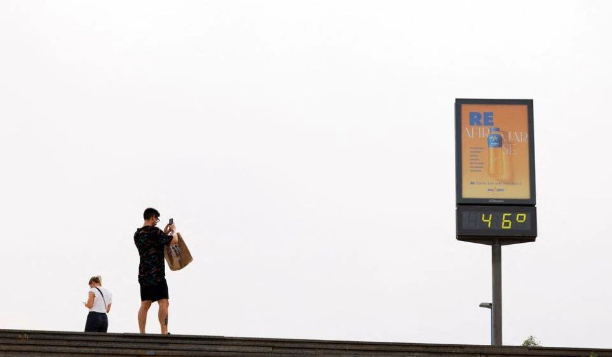A man takes a picture of a thermometer displaying 46 Celsius degrees
